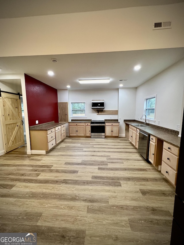 kitchen featuring appliances with stainless steel finishes, built in desk, light brown cabinetry, kitchen peninsula, and a barn door