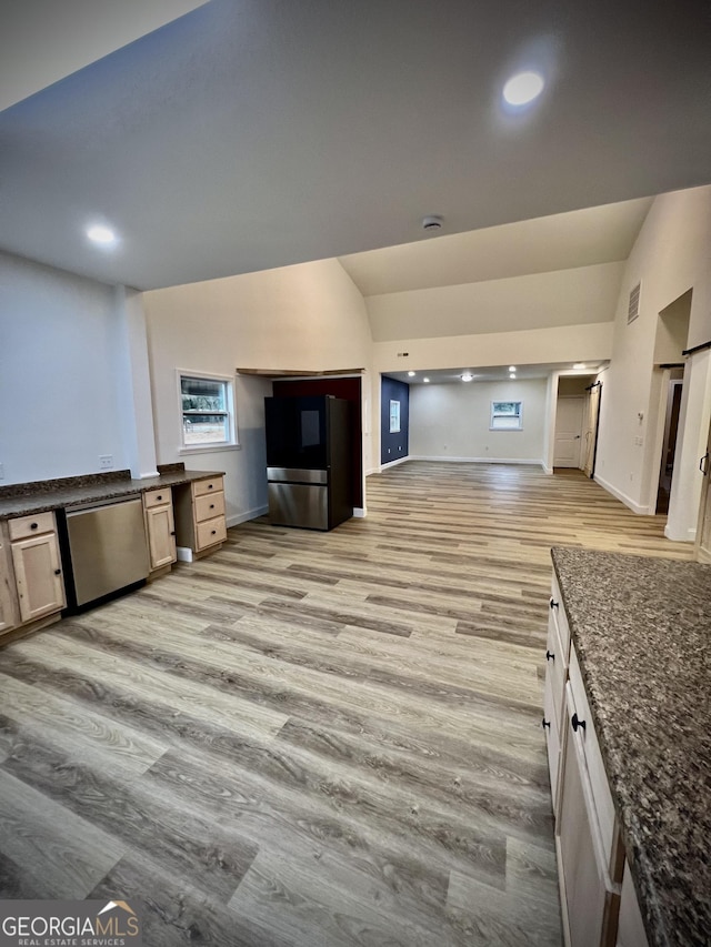 kitchen featuring appliances with stainless steel finishes, light hardwood / wood-style floors, vaulted ceiling, and dark stone countertops