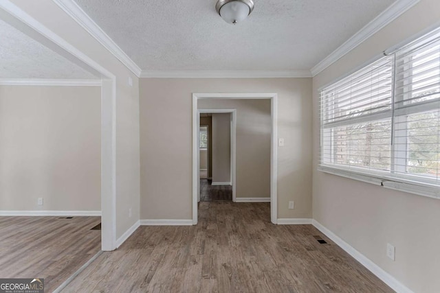 spare room with ornamental molding, a textured ceiling, and light hardwood / wood-style flooring