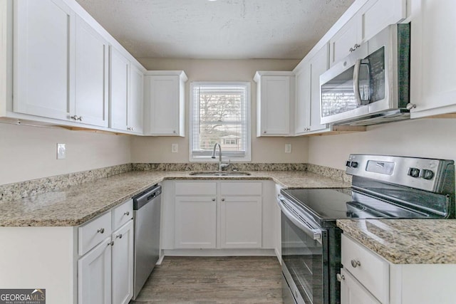 kitchen featuring sink, white cabinetry, a textured ceiling, appliances with stainless steel finishes, and light hardwood / wood-style floors