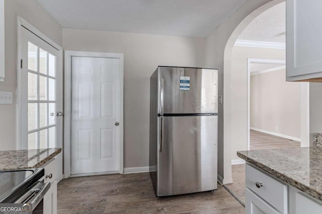 kitchen featuring dark wood-type flooring, light stone counters, a textured ceiling, stainless steel refrigerator, and white cabinets