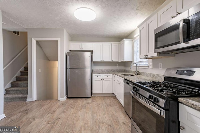 kitchen with sink, white cabinetry, stainless steel appliances, light stone countertops, and a textured ceiling