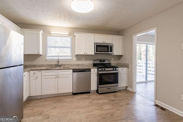 kitchen featuring white cabinetry, sink, stainless steel appliances, a textured ceiling, and light hardwood / wood-style flooring