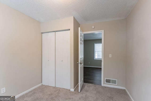 unfurnished bedroom with a closet, light carpet, and a textured ceiling