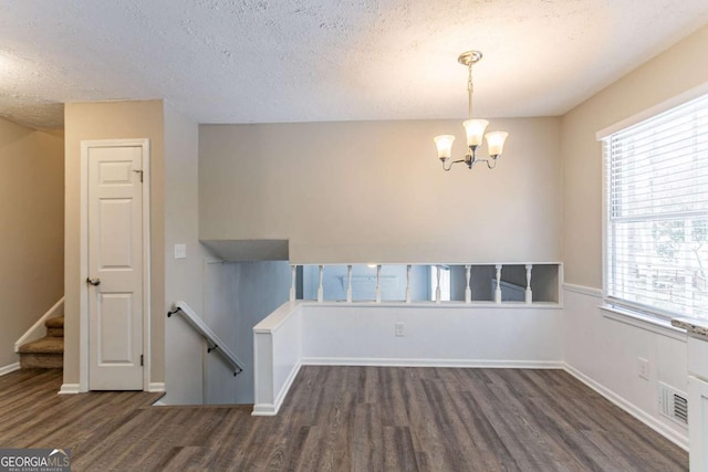 spare room with a healthy amount of sunlight, an inviting chandelier, a textured ceiling, and dark hardwood / wood-style flooring