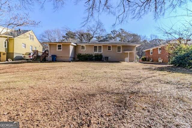 rear view of house with central AC unit and a lawn