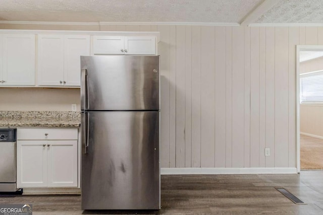 kitchen featuring appliances with stainless steel finishes, wood walls, white cabinets, light stone counters, and a textured ceiling