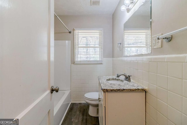 full bathroom featuring tile walls, hardwood / wood-style flooring, vanity, toilet, and a textured ceiling