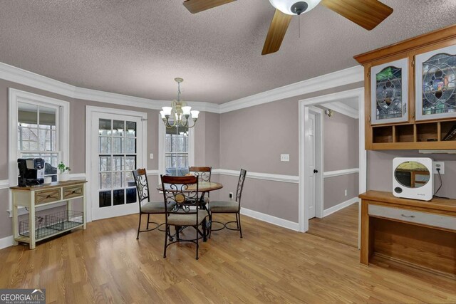 dining space with ceiling fan with notable chandelier, ornamental molding, light hardwood / wood-style floors, and a textured ceiling