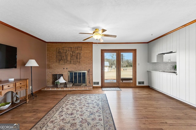 living room featuring crown molding, a fireplace, a textured ceiling, and light wood-type flooring