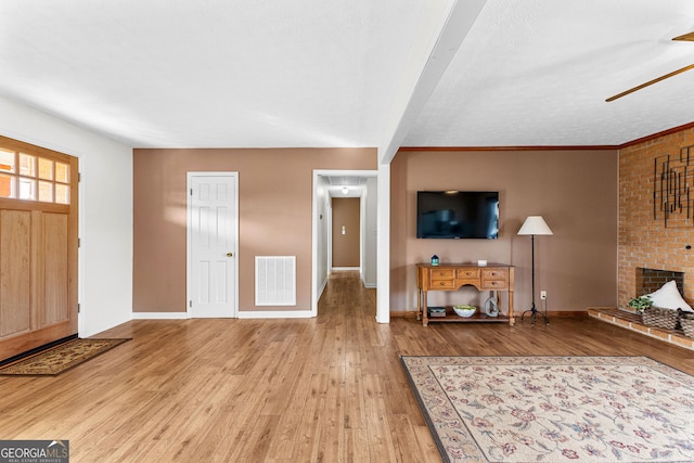 living room with a brick fireplace, a textured ceiling, beamed ceiling, ceiling fan, and hardwood / wood-style floors