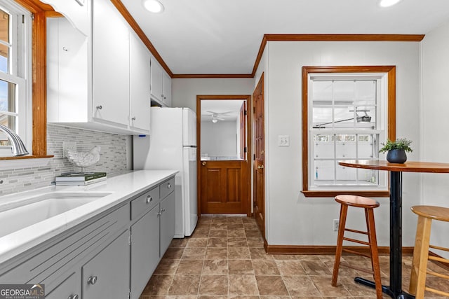 kitchen featuring sink, white refrigerator, ornamental molding, white cabinets, and decorative backsplash