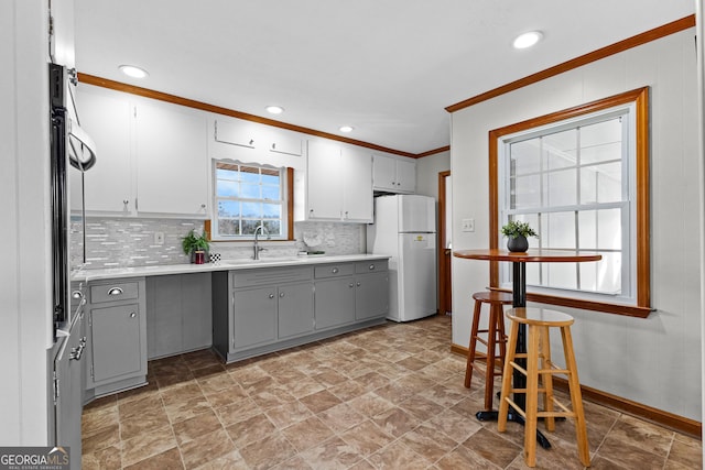 kitchen with sink, gray cabinetry, crown molding, white fridge, and backsplash