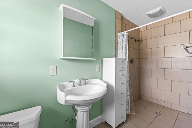 bathroom featuring a shower with curtain, tile patterned floors, a textured ceiling, and toilet