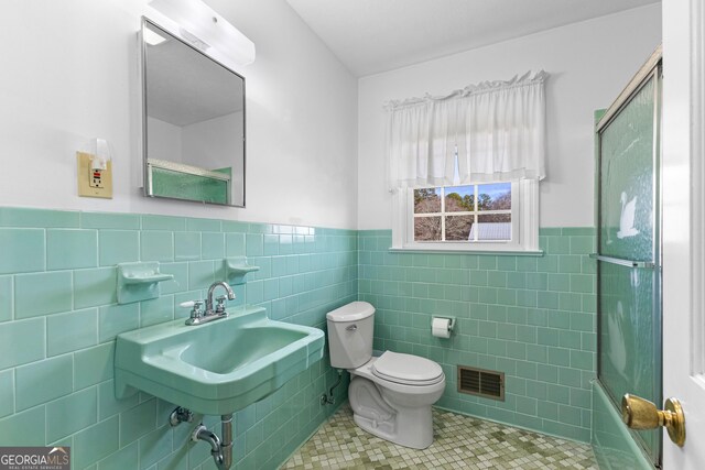 full bathroom featuring toilet, tile patterned floors, shower / bath combination with glass door, and tile walls