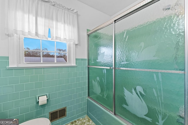 bathroom featuring tile walls, shower / bath combination with glass door, and toilet