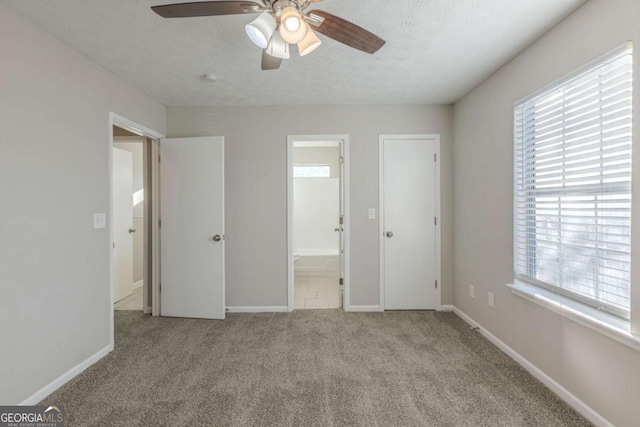 unfurnished bedroom featuring connected bathroom, a textured ceiling, light colored carpet, and ceiling fan