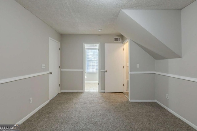 additional living space featuring light colored carpet and a textured ceiling