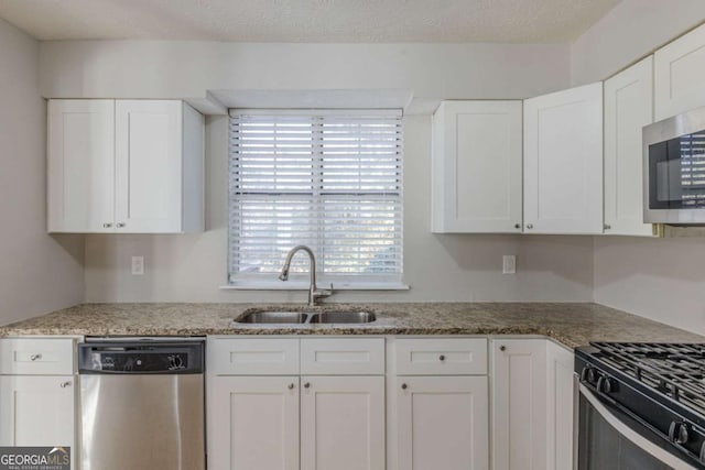 kitchen featuring stone counters, white cabinetry, sink, stainless steel appliances, and a textured ceiling