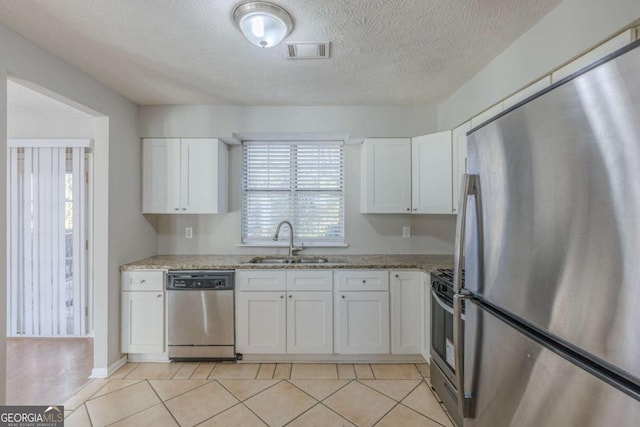 kitchen with sink, appliances with stainless steel finishes, light stone countertops, a textured ceiling, and white cabinets