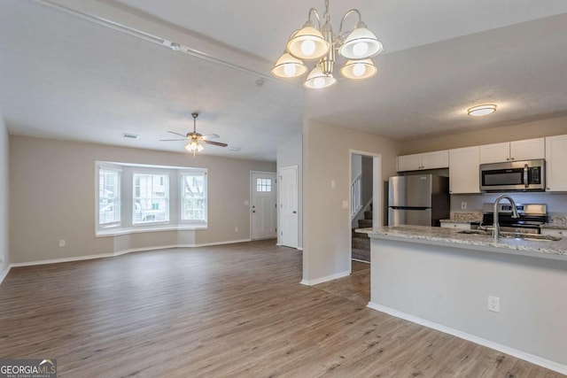 kitchen featuring decorative light fixtures, light hardwood / wood-style flooring, appliances with stainless steel finishes, light stone countertops, and white cabinets