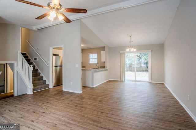 unfurnished living room featuring vaulted ceiling with beams, ceiling fan with notable chandelier, light hardwood / wood-style floors, and sink