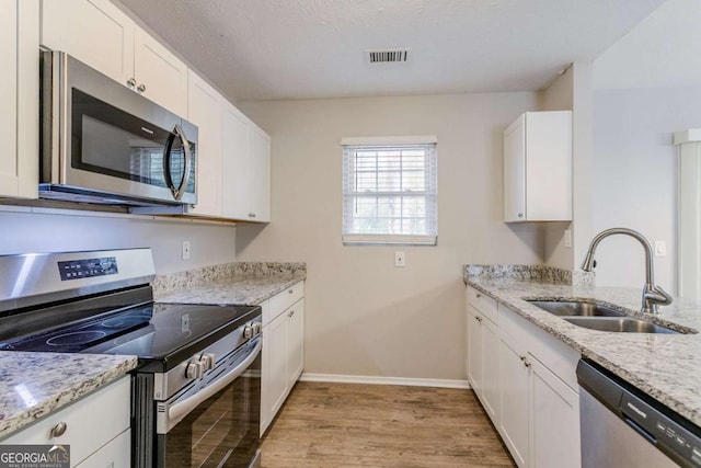 kitchen with sink, stainless steel appliances, light stone countertops, white cabinets, and light wood-type flooring