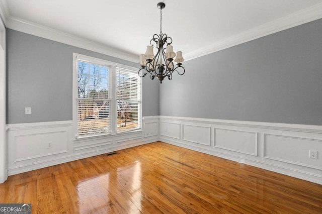 unfurnished dining area with hardwood / wood-style flooring, ornamental molding, and a chandelier