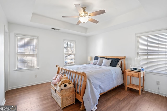 bedroom with dark wood-type flooring, ceiling fan, and a tray ceiling