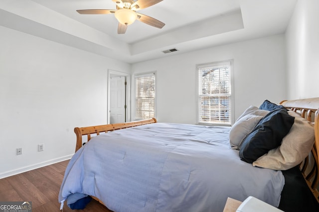 bedroom with a tray ceiling, dark hardwood / wood-style floors, and ceiling fan