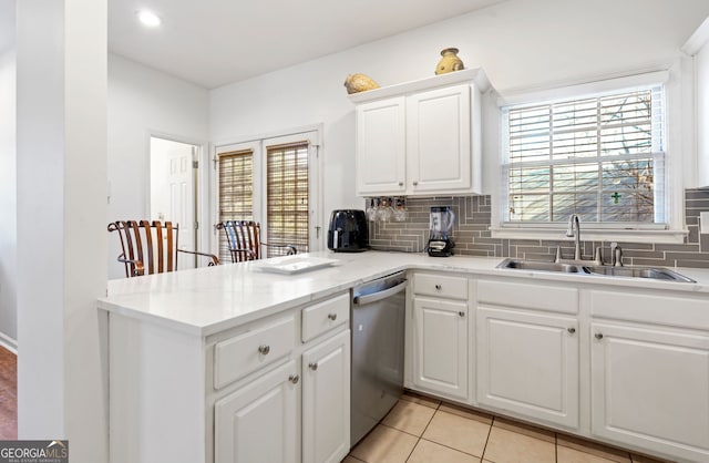 kitchen with sink, light tile patterned floors, dishwasher, white cabinets, and decorative backsplash