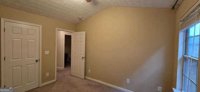 unfurnished bedroom with ceiling fan, lofted ceiling, light carpet, and a textured ceiling