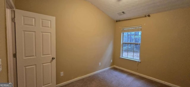 carpeted empty room featuring vaulted ceiling and a textured ceiling