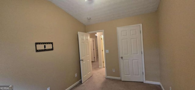 unfurnished bedroom featuring vaulted ceiling, light carpet, and a textured ceiling