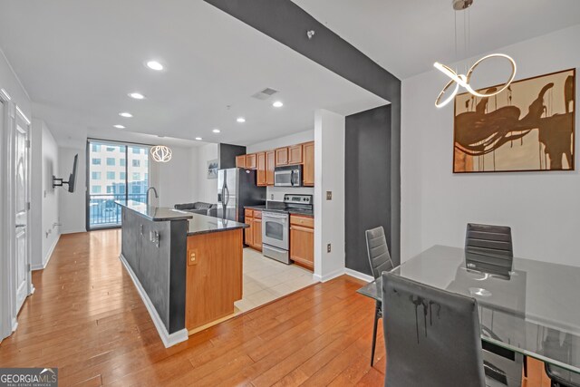 kitchen with a kitchen breakfast bar, hanging light fixtures, stainless steel appliances, a center island with sink, and light wood-type flooring