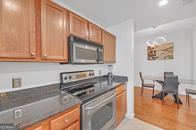 kitchen featuring appliances with stainless steel finishes, dark stone countertops, light hardwood / wood-style floors, and decorative light fixtures