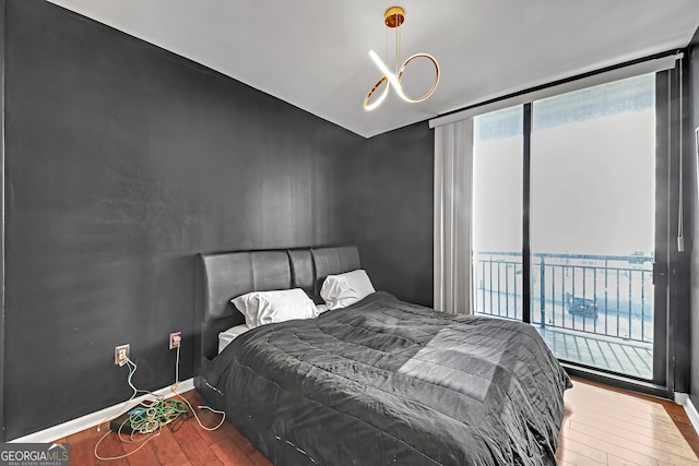 bedroom with a water view, a wall of windows, access to outside, and hardwood / wood-style flooring