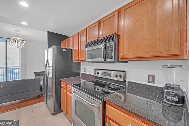 kitchen with an inviting chandelier, stainless steel appliances, light tile patterned flooring, decorative light fixtures, and dark stone counters