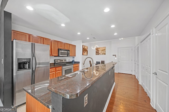 kitchen with sink, a center island with sink, dark stone counters, stainless steel appliances, and light hardwood / wood-style floors