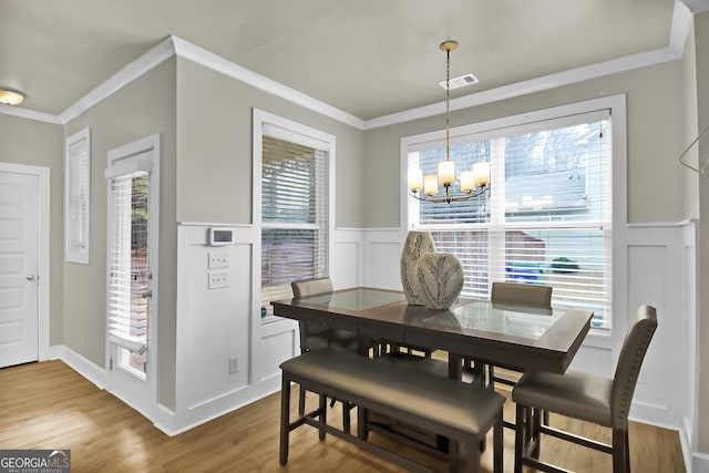 dining space with an inviting chandelier, wood-type flooring, and ornamental molding