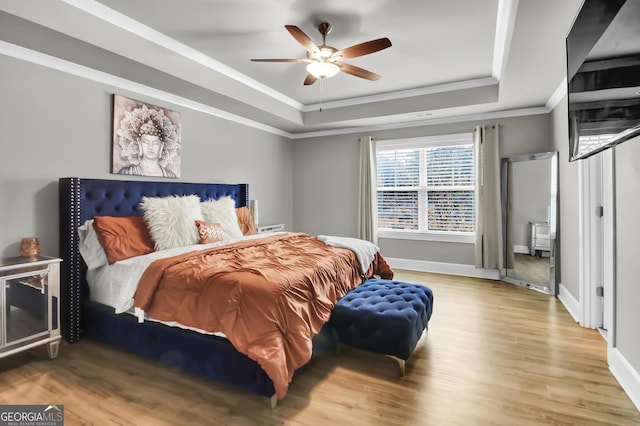 bedroom featuring crown molding, wood-type flooring, a raised ceiling, and ceiling fan