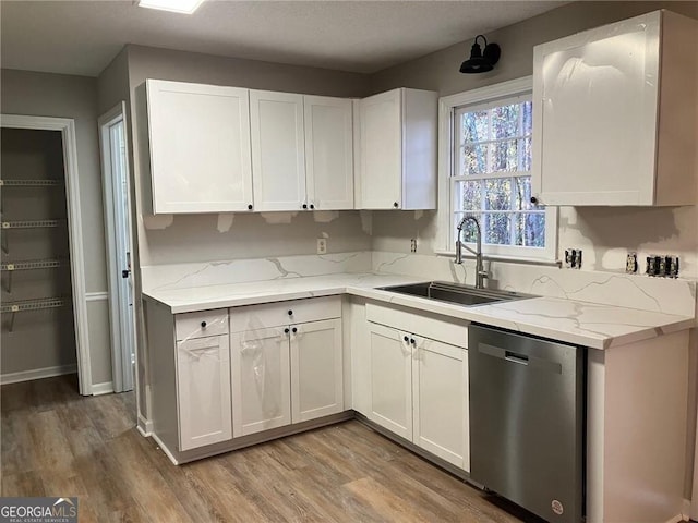 kitchen featuring sink, white cabinetry, light stone counters, stainless steel dishwasher, and light hardwood / wood-style floors