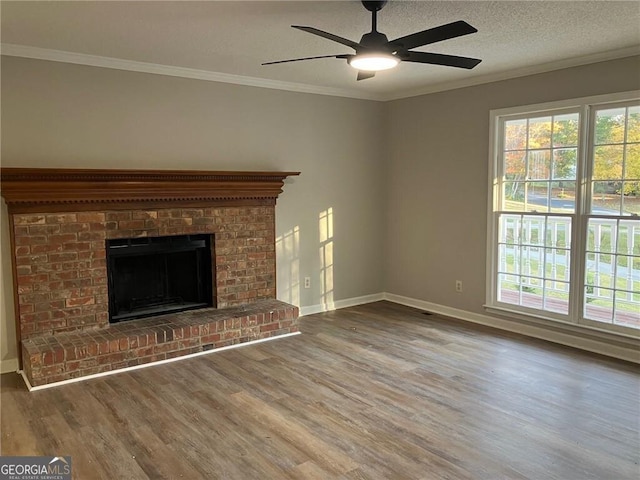 unfurnished living room with hardwood / wood-style flooring, ceiling fan, crown molding, a brick fireplace, and a textured ceiling