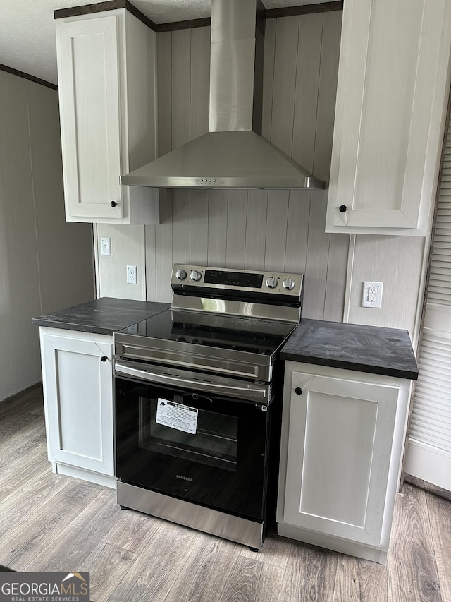 kitchen featuring white cabinetry, wall chimney exhaust hood, light hardwood / wood-style flooring, and electric range