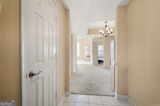 hallway with light colored carpet, a textured ceiling, and a notable chandelier