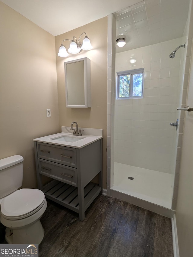 bathroom with wood-type flooring, a tile shower, vanity, and toilet