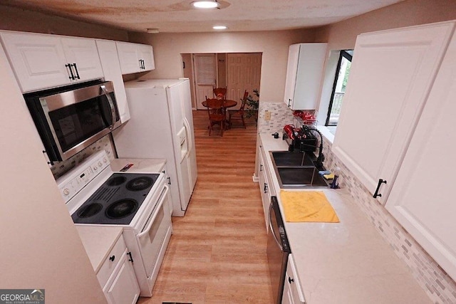 kitchen featuring sink, light wood-type flooring, electric stove, decorative backsplash, and white cabinets