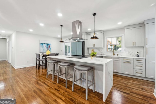 kitchen with hanging light fixtures, a center island, island range hood, wood-type flooring, and decorative backsplash