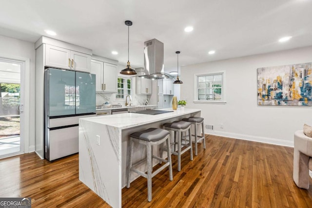 kitchen featuring island range hood, refrigerator, sink, white cabinets, and hanging light fixtures