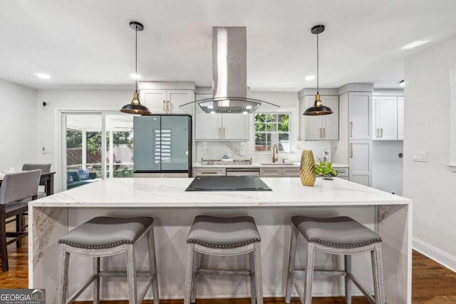 kitchen featuring light stone counters, island range hood, a kitchen bar, and hanging light fixtures